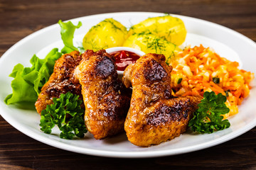 Fried chicken wings with boiled potatoes and vegetable salad on wooden board