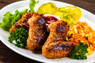 Fried chicken wings with boiled potatoes and vegetable salad on wooden board