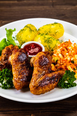 Fried chicken wings with boiled potatoes and vegetable salad on wooden board