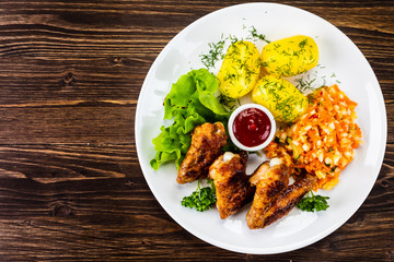 Fried chicken wings with boiled potatoes and vegetable salad on wooden board