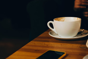 Photo of cup of coffee on table in restaurant near smartphone, morning concept