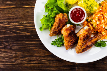 Fried chicken wings with boiled potatoes and vegetable salad on wooden board
