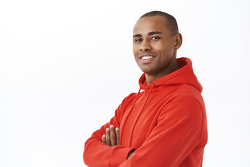 Close-up portrait of young successful african-american adult man in red hoodie, cross arms on chest turn head to camera with satisfied smile, looking confident and reliable, white background