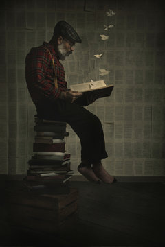 Man sitting on a pile of books reading a book letting go of the imagination Surreal image. Vertical image
