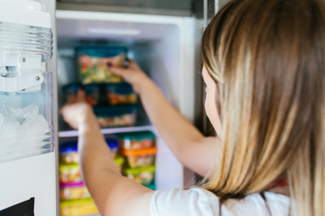 Fototapeta na wymiar Woman placing container with frozen mixed vegetables in freezer.