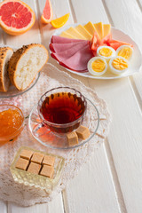 Fresh delicious breakfast with soft boiled egg, cheese, ham fresh bread and cup coffee or tea on light wooden background.