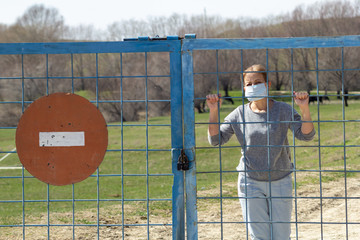 Caucasian women stand in protective mask behind closed gate with red stop sign. in quarantine for coronavirus covid-19 . Stay at home concept