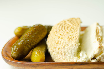 Smoked cottage cheese, brined cheese cut with pickled cucumber on a wooden plate