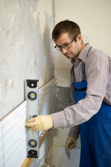 A man in overalls is leveling the walls in the kitchen to lay ceramic tiles on the gray cement on the wall.
