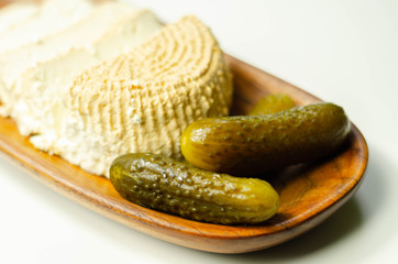 Smoked cottage cheese, brined cheese cut with pickled cucumber on a wooden plate