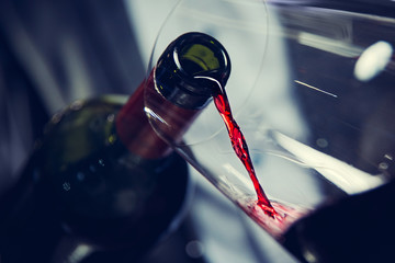 Pouring red wine move into glass against dark background