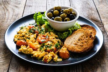 Breakfast - scrambled eggs with vegetables and toasted bread on wooden background