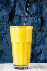 Yellow smoothie (orange, mandarin) in a large glass cup against a dark wall.