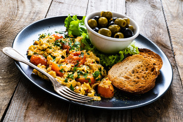 Breakfast - scrambled eggs with vegetables and toasted bread on wooden background