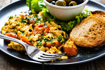 Breakfast - scrambled eggs with vegetables and toasted bread on wooden background