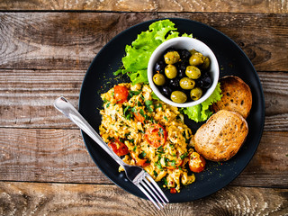 Breakfast - scrambled eggs with vegetables and toasted bread on wooden background