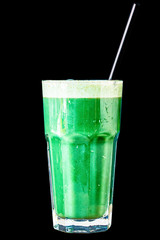 Green smoothie made from herbs and vegetables in a large glass glass on a black background, isolated