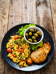 Breakfast - scrambled eggs with vegetables and toasted bread on wooden background