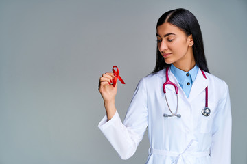 Girl in a medical coat with a phonendoscope on her shoulders with a red ribbon in her hand with red...