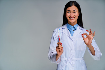 Female doctor with a phonendoscope in a white medical coat shows a toothbrush and two fingers in circle. Dental concept