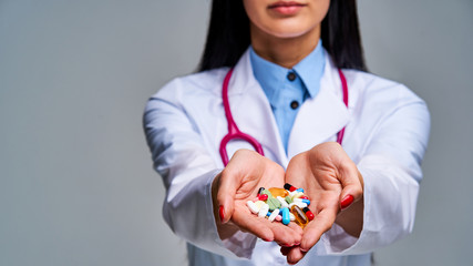 Female doctor with a phonendoscope on her neck holds and shows a handful of pills in her palms. Medical concept