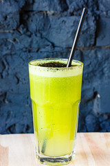 Green smoothie made from herbs and vegetables in a large glass glass against a dark stone wall