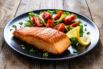 Fried salmon steaks with vegetables on wooden table