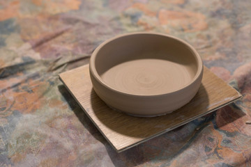 Unpainted clay plate on the table. Beige plate earthenware standing on table in pottery workshop