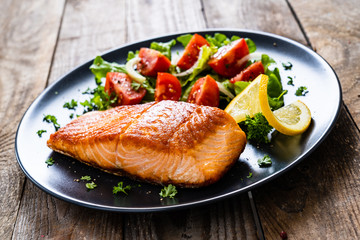 Fried salmon steaks with vegetables on wooden table