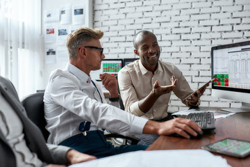 Forward thinking. Successful businessmen trading stocks. Stock traders looking at graphs, indexes and numbers on multiple computer screens. Two colleagues in modern office