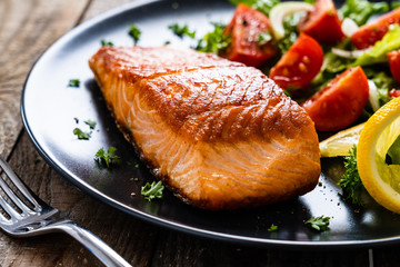 Fried salmon steaks with vegetables on wooden table