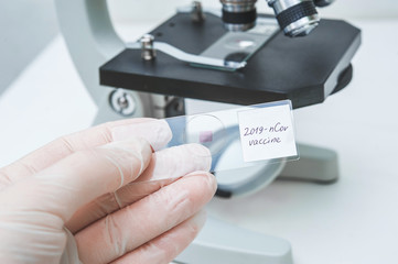 a human hand in a disposable glove holds a medical glass for a microscope with a coronavirus vaccine sample. vaccine inscription. drug development