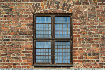 Antique Old wooden window with metal fittings and hinges in old red brick wall of an ancient European castle.