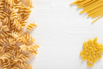 Uncooked dried pasta selection on wooden white background. Free space for text. Top view.