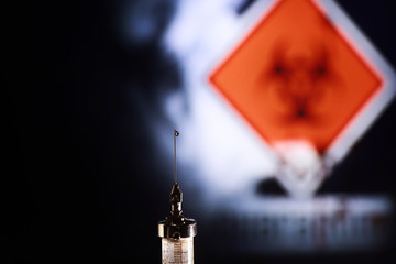 Medical syringe with a needle and a cure for the virus. A drop of drug flows down the needle....