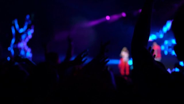 4K People jumping cheering clapping at live musical performance. Bright flashlights shooting off stage. Entertainment, live music concept.