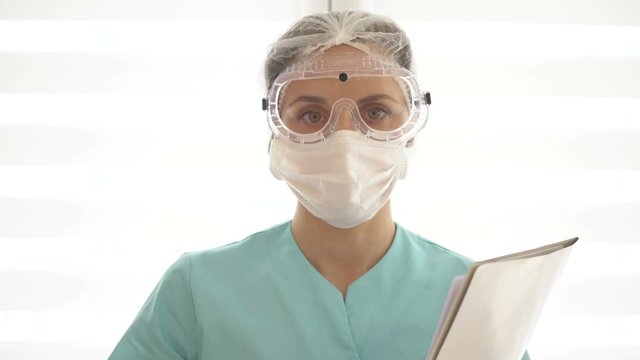 Young nurse or woman doctor in a medical mask, goggles and disposable gloves. She makes a warning gesture.