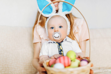 Happy Easter. A mother and a baby with rabbit ears on Easter day, with Easter colored eggs having fun. Family celebrates Easter