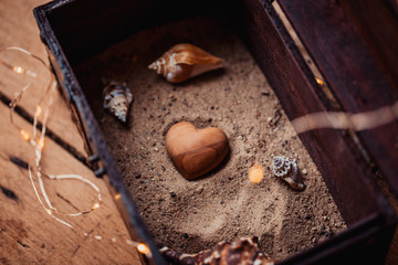 Liebe, Schatz, Schatztruhe - Herz aus Holz in Sand mit Muscheln in Schatztruhe
