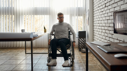 Portrait of young male office worker in a wheelchair moving around in modern bright office.