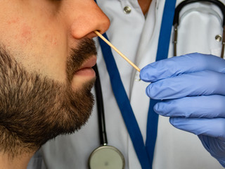 Quick test for suspected coronavirus diagnosis.  Physician taking a nasofaringeal sample of an adult bearded man, with a cotton swab. Covid19 screening.