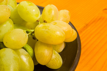 large brush of green grapes in a dark ceramic plate on a wooden background