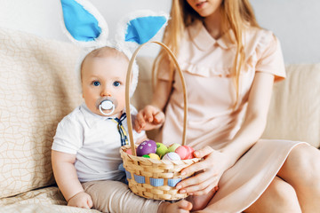 Happy Easter. A mother and a baby with rabbit ears on Easter day, with Easter colored eggs having fun. Family celebrates Easter