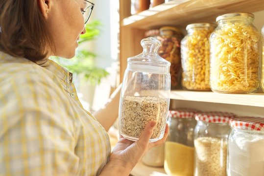 Food storage in pantry, woman holding jar of oatmeal in hand - Powered by Adobe