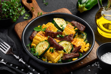 Delicious salad with beef, corn, zucchini and micro greens in a black plate on a dark background. Healthy food. Close-up. Selective focus.
