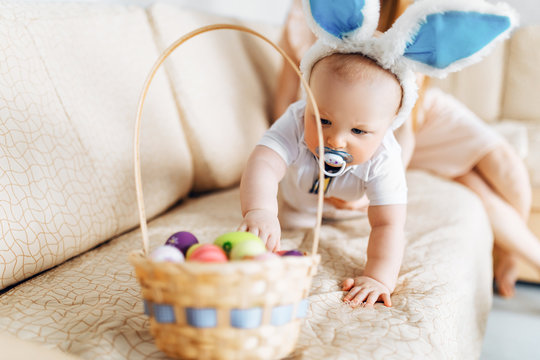 Cute funny baby with rabbit ears and a basket full of Easter eggs at home