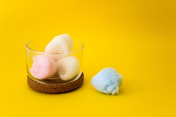 colored cotton wool ball inside glass small container with wooden top. Yellow background. Free copy space. Hygiene