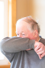 Elderly man coughing into his elbow to avoid spreading virus, germs and air born droplets amid coronavirus, Covid-19. 