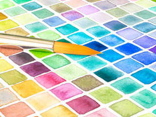 Art brush over a color pallet painted with watercolor