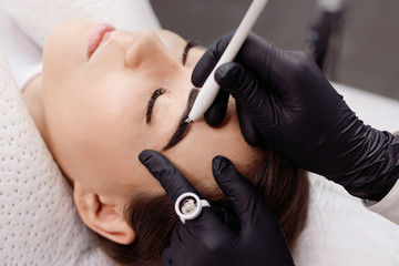 Beautiful young girl with long eyelashes tweezing her eyebrows in a beauty salon. Woman doing eyebrow permanent makeup correction. Microblading brow.